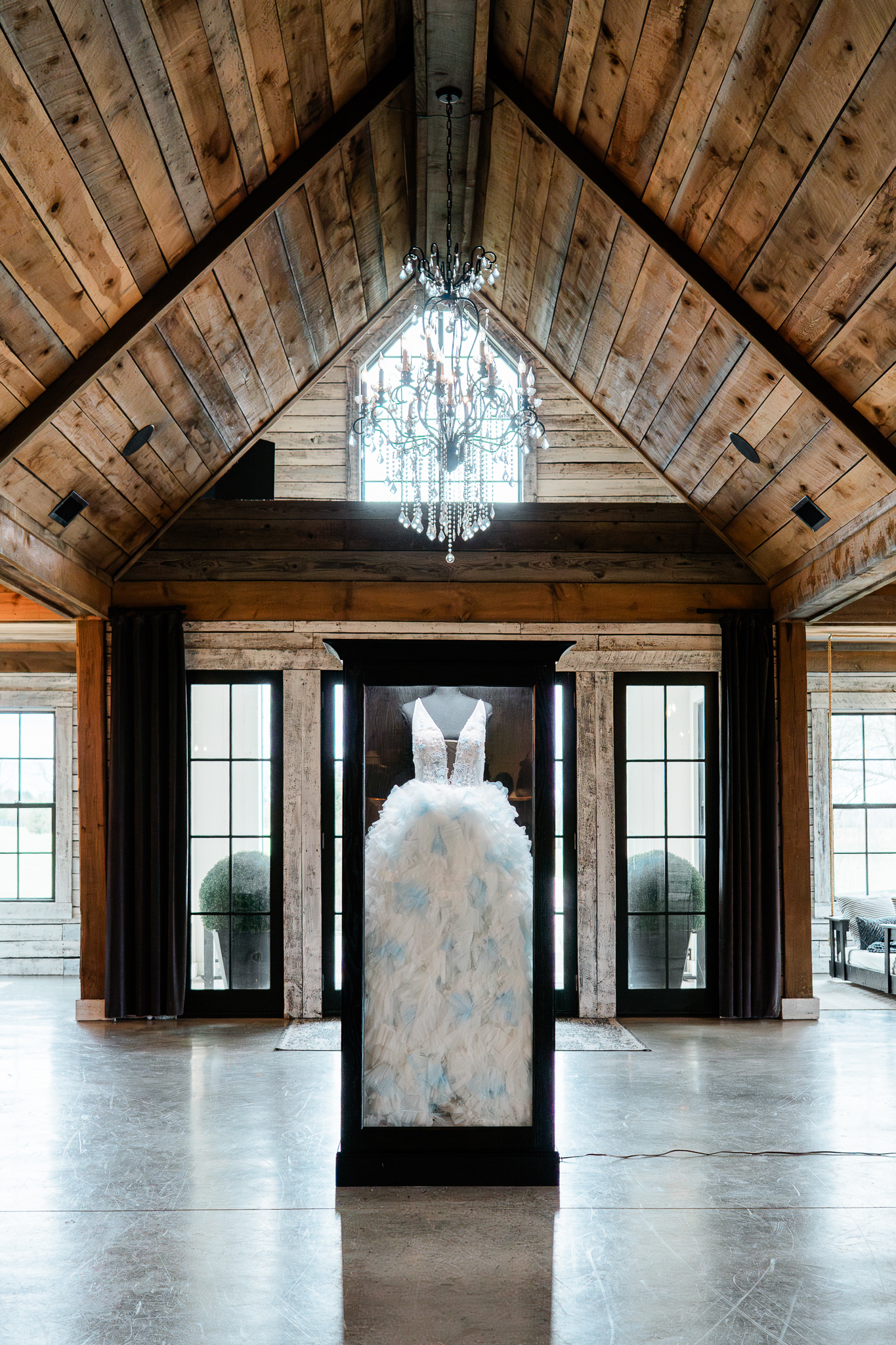A freestanding Mrs. Case Signature displaying a lace gown in a timber hall